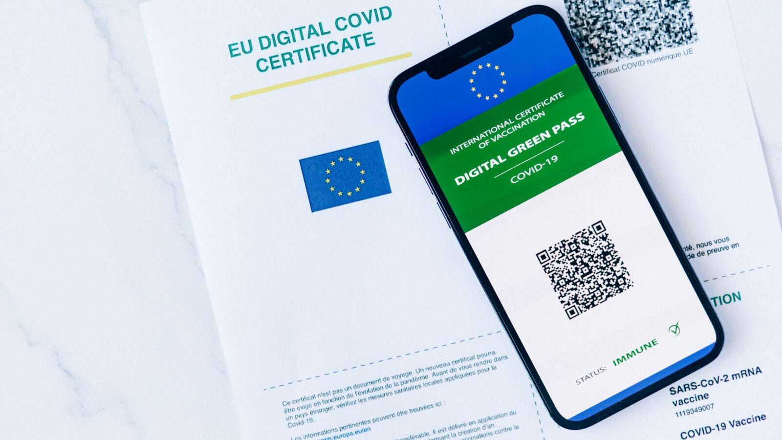 Smartphone con schermata "DIGITAL GREEN PASS - COVID-19" e QR code, appoggiato su un foglio "EU DIGITAL COVID CERTIFICATE"