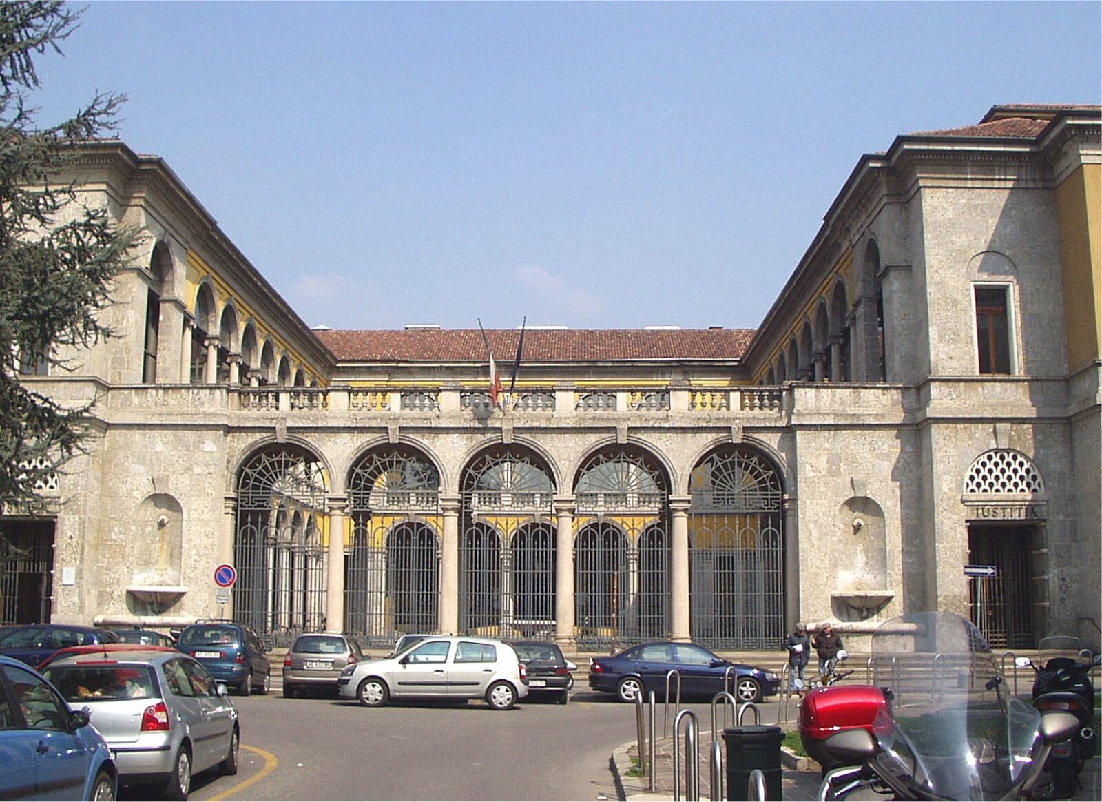 Facciata in pietra del Palazzo di Giustizia di Monza con portici ad arco, bandiera italiana e auto parcheggiate sulla piazza