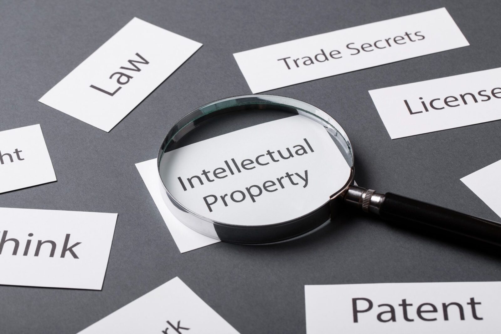 Lente d'ingrandimento su un foglietto con scritto "Intellectual Property", tra bigliettini con "Law", "Trade Secrets", "Patent"