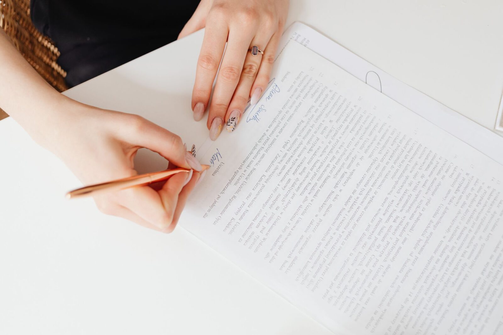Mani di una persona che firmano con una penna dorata un documento di più pagine appoggiato su un tavolo bianco