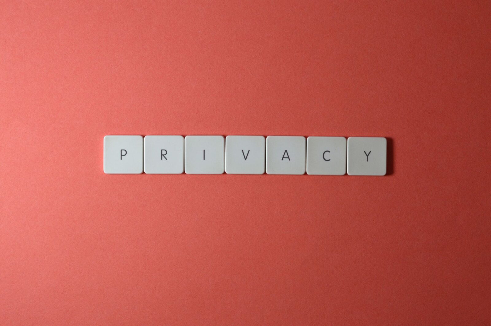 Tessere bianche con lettere nere allineate su fondo rosso corallo compongono la parola PRIVACY al centro dell'inquadratura