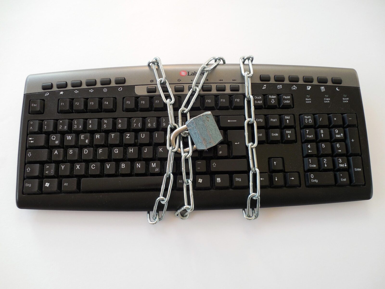 Tastiera di computer nera con layout QWERTZ avvolta da una catena metallica chiusa da un lucchetto, su sfondo bianco