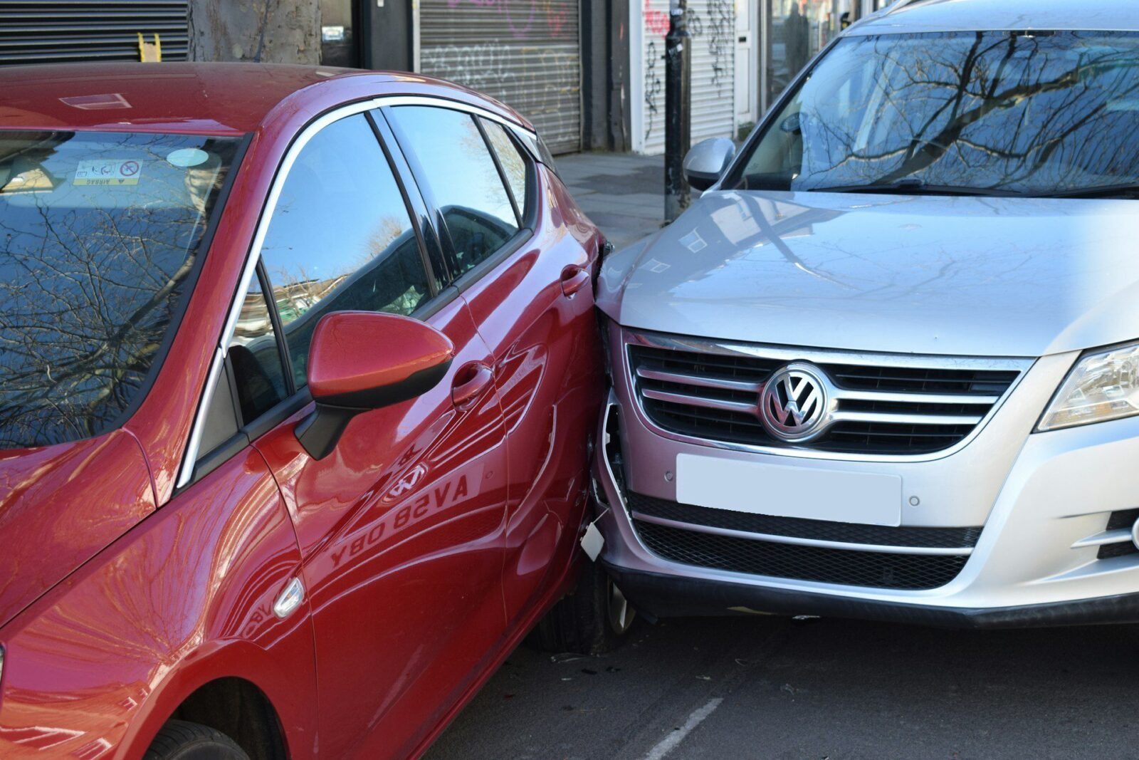 Tamponamento tra due auto in strada: la fiancata ammaccata di una vettura rossa contro il muso di una Volkswagen grigia